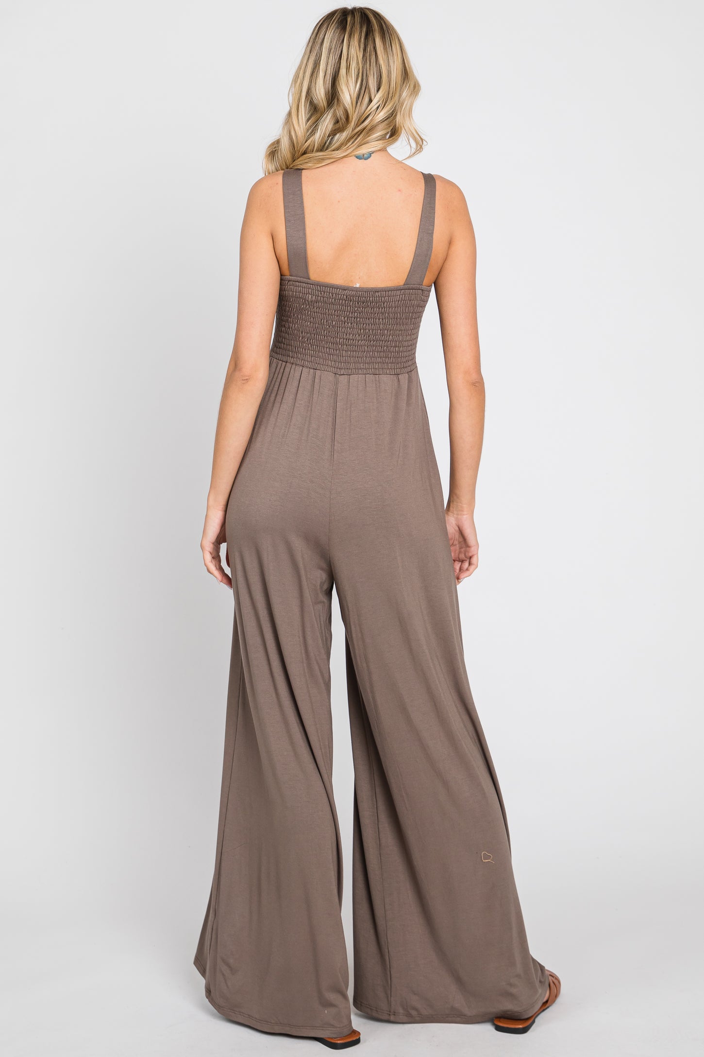 woman wearing a brown sleeveless backless jumpsuit with wide leg pants and a smocked bodice