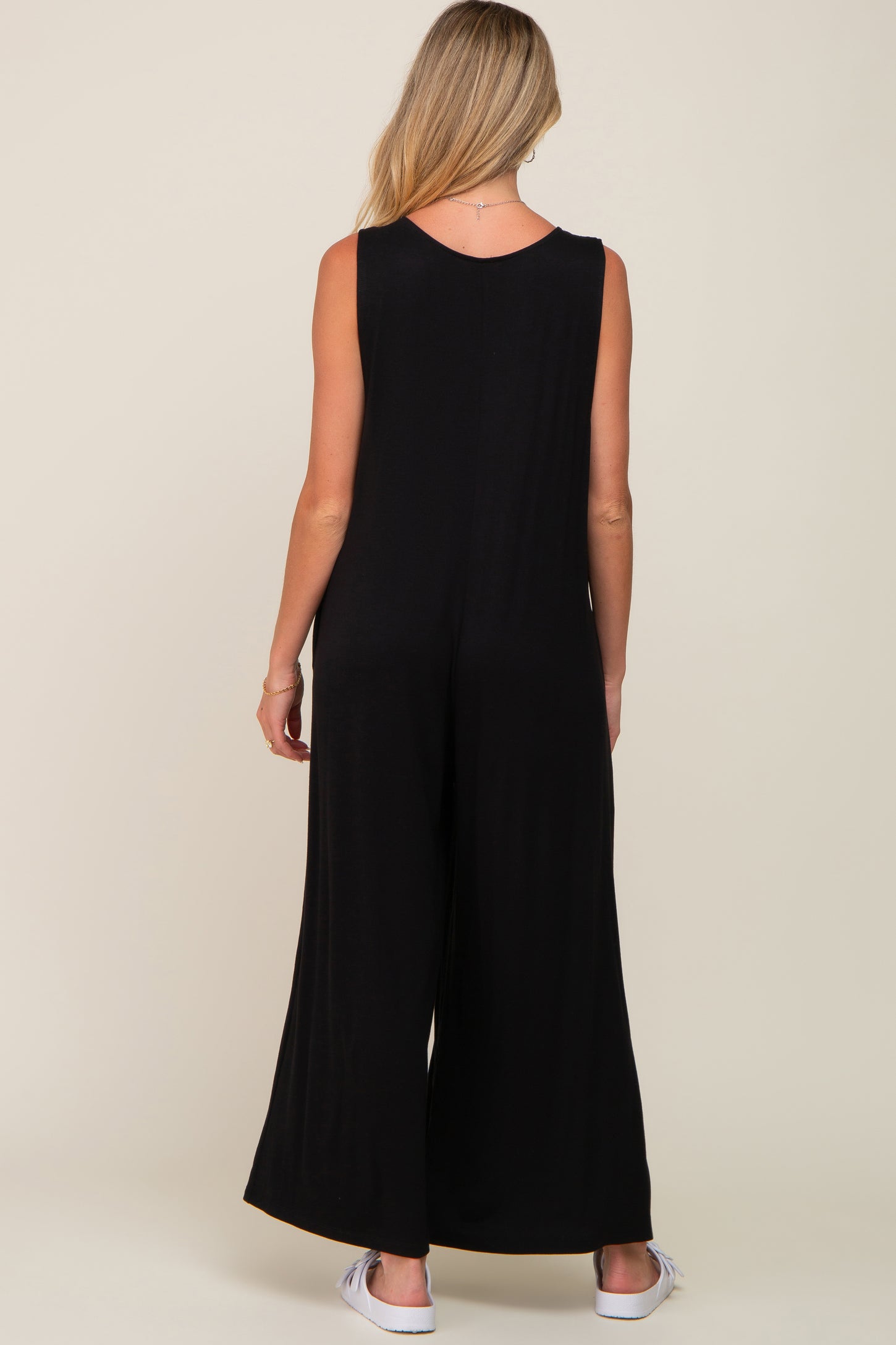 woman wearing a black sleeveless maternity jumpsuit, showing a relaxed fit and wide leg style from the back