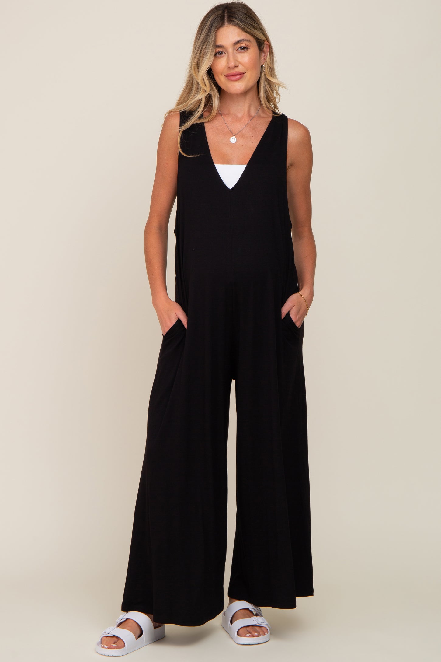 woman wearing a black sleeveless maternity jumpsuit with pockets, showing a visible baby bump