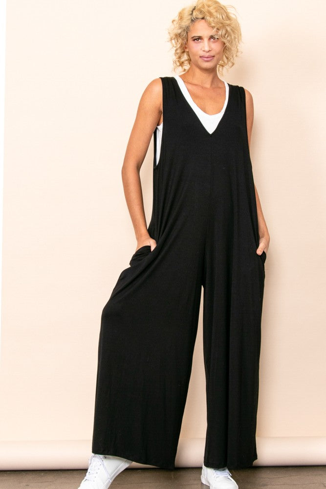 woman wearing a black sleeveless jumpsuit with deep pockets and a loose fit, paired with white sneakers