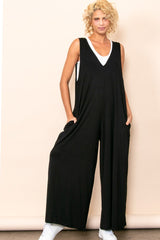 woman wearing a black sleeveless jumpsuit with deep pockets and a loose fit, paired with white sneakers