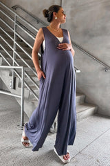 woman wearing a gray sleeveless maternity jumpsuit, displaying her baby bump, standing on a staircase