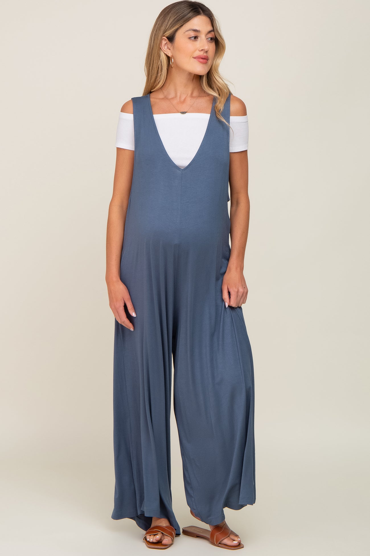 woman wearing a navy blue maternity jumpsuit with wide legs and an off-the-shoulder white top, showing a baby bump