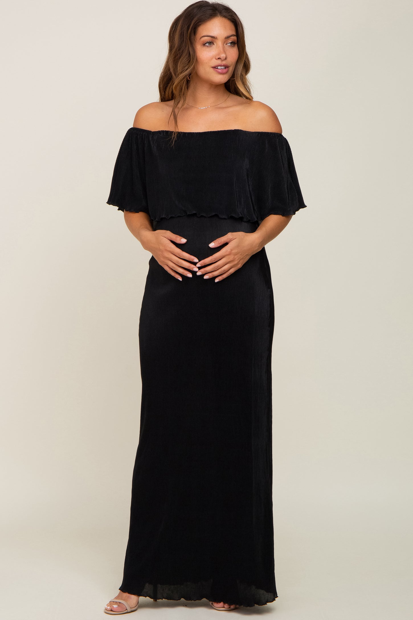 woman wearing a black off-the-shoulder maternity dress with a flowy top and holding her baby bump