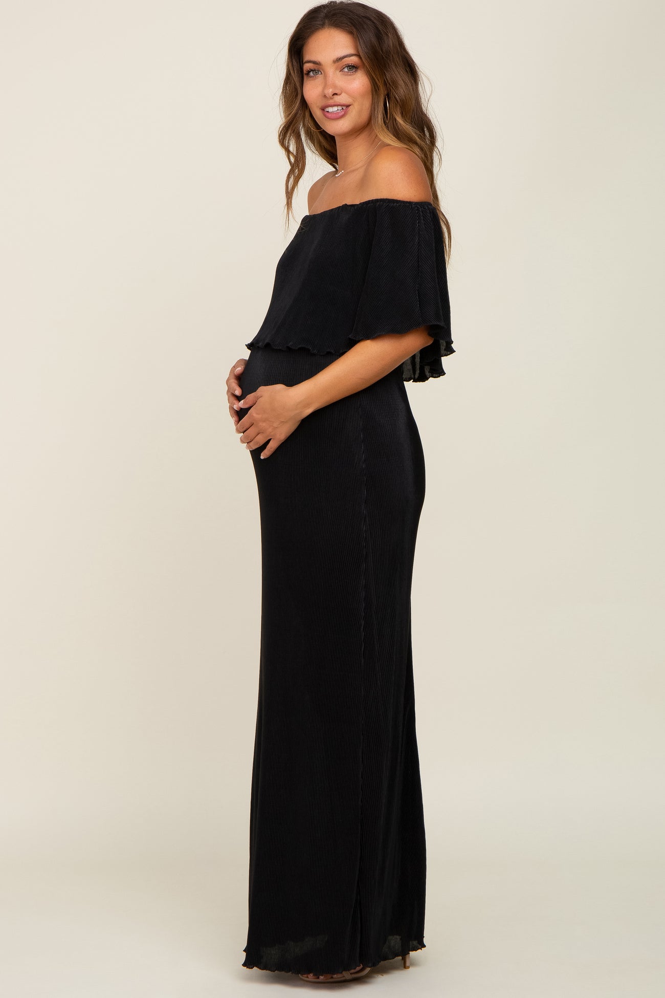 woman wearing a black off-the-shoulder maternity dress and holding her baby bump