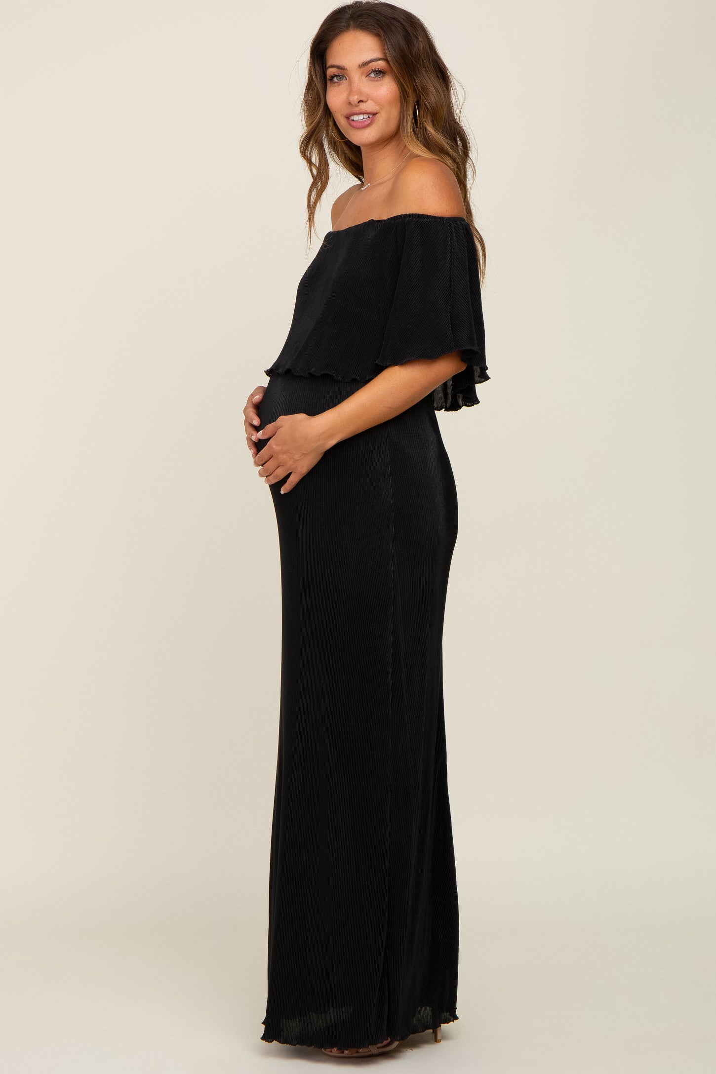 woman wearing a black off-the-shoulder maternity dress and holding her baby bump