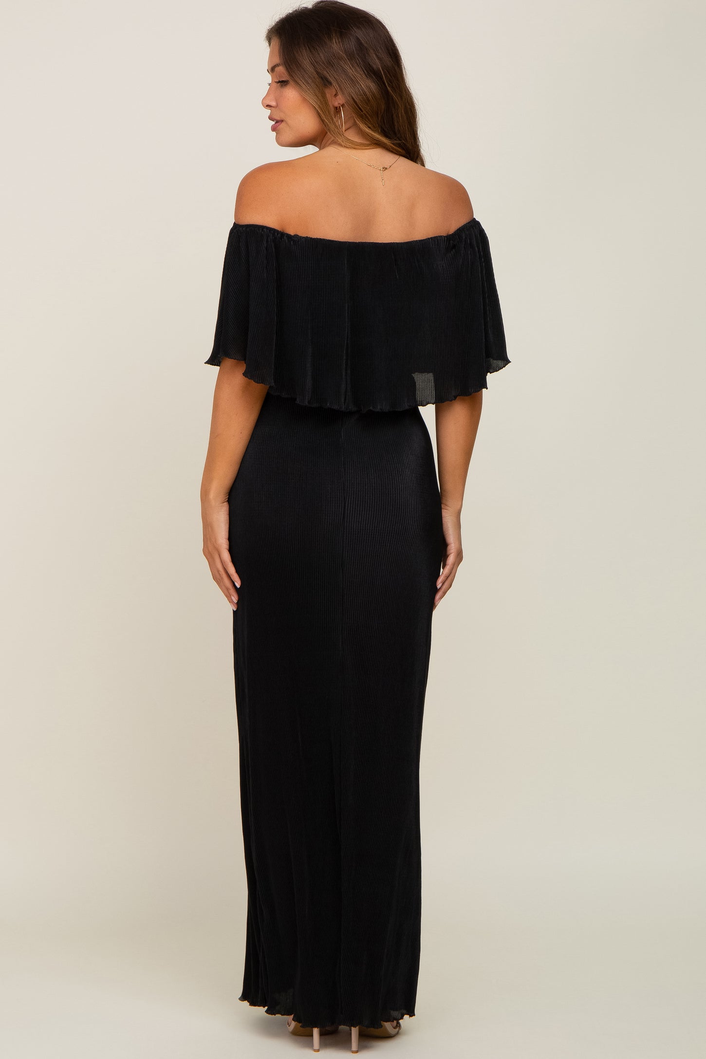 woman wearing a black off-the-shoulder pleated maternity maxi dress with a flowy top detail, viewed from the back