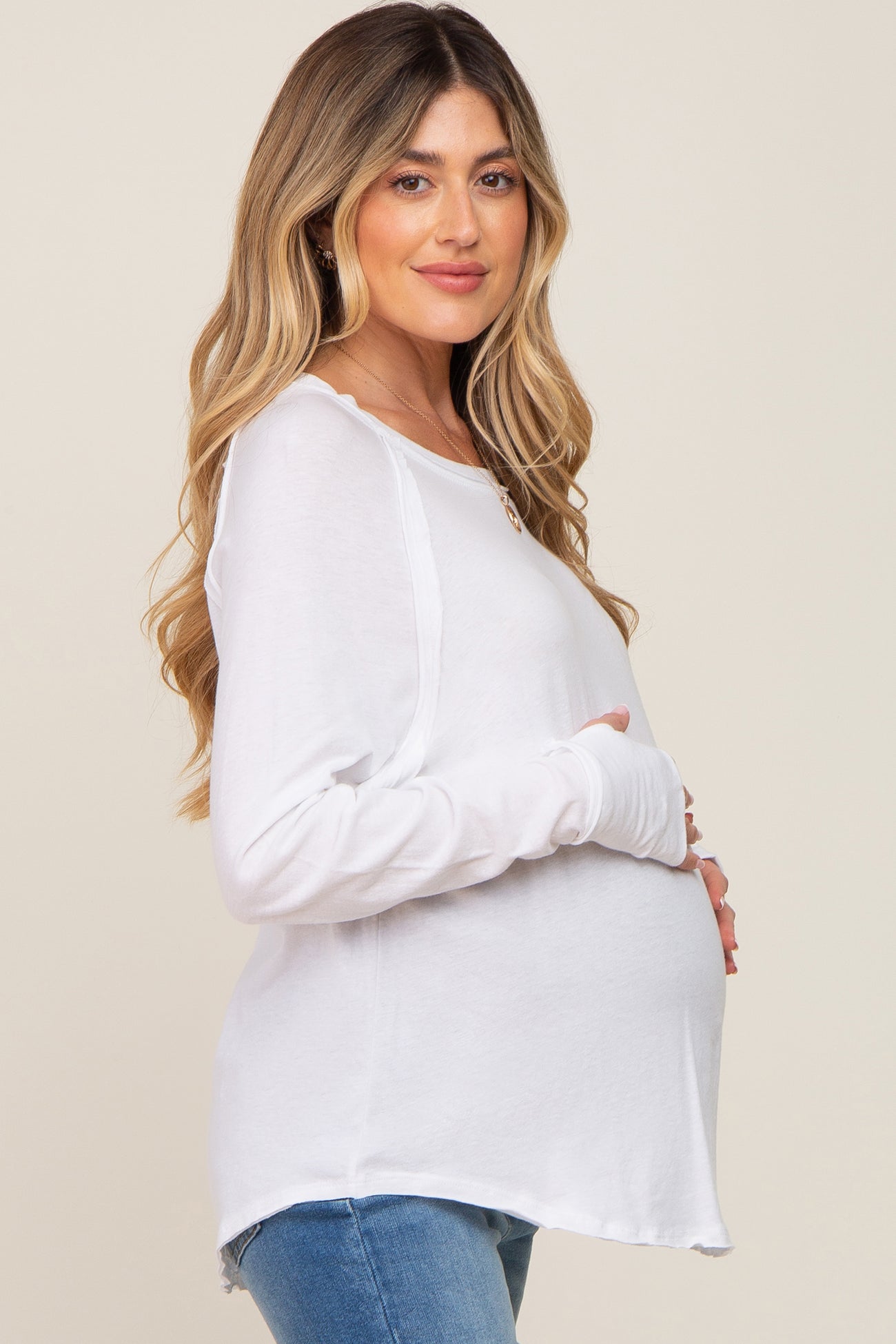 woman wearing a white long sleeve maternity top and cradling her baby bump