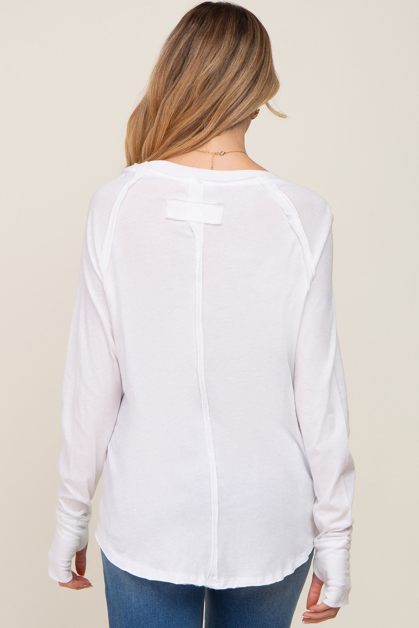 woman wearing a white long sleeve maternity top with a relaxed fit and back detail, styled with blue jeans