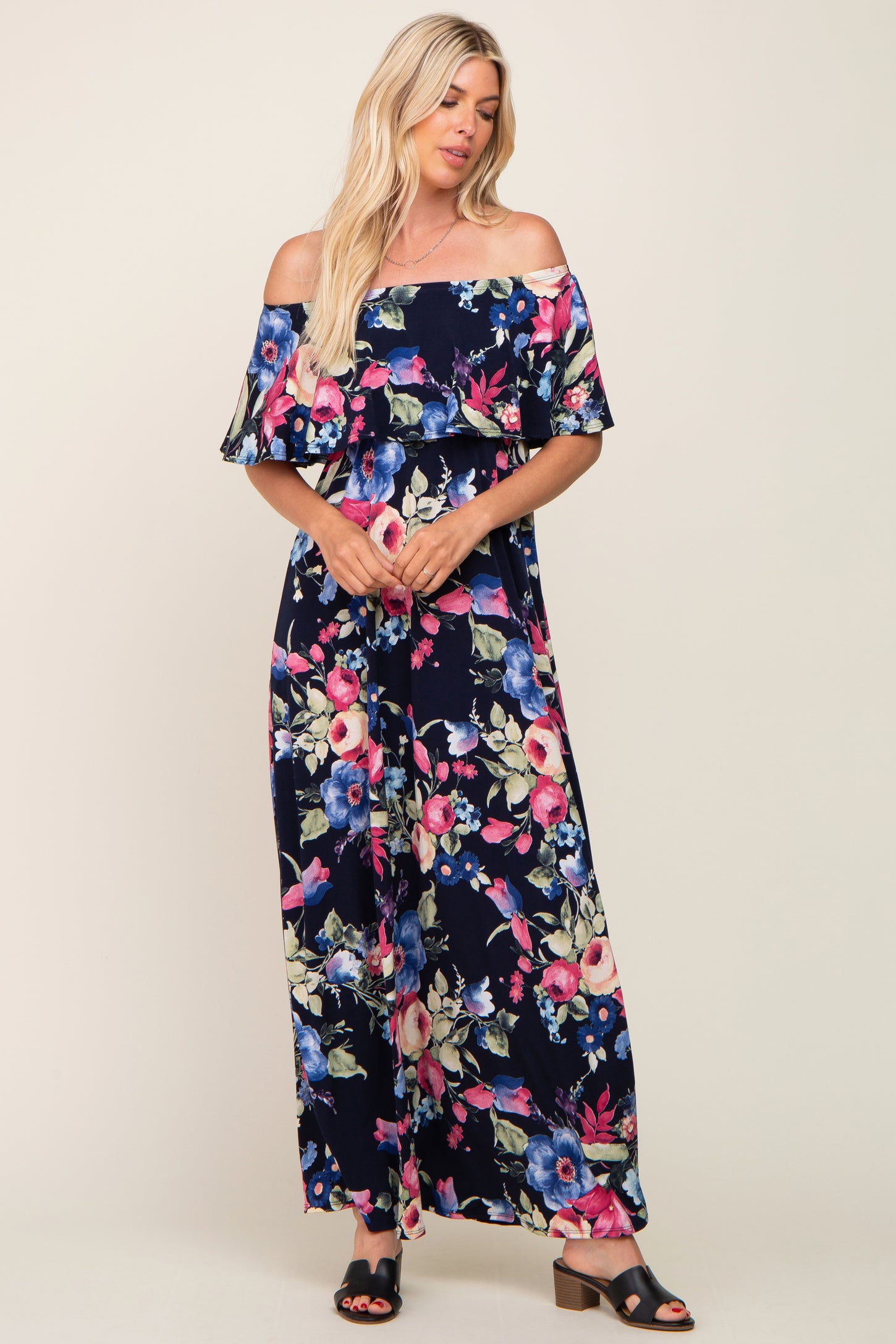 woman wearing a navy blue off-the-shoulder floral maxi dress with ruffle detail and black strappy sandals