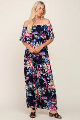 woman wearing a navy blue off-the-shoulder floral maxi dress with ruffle detail and black strappy sandals