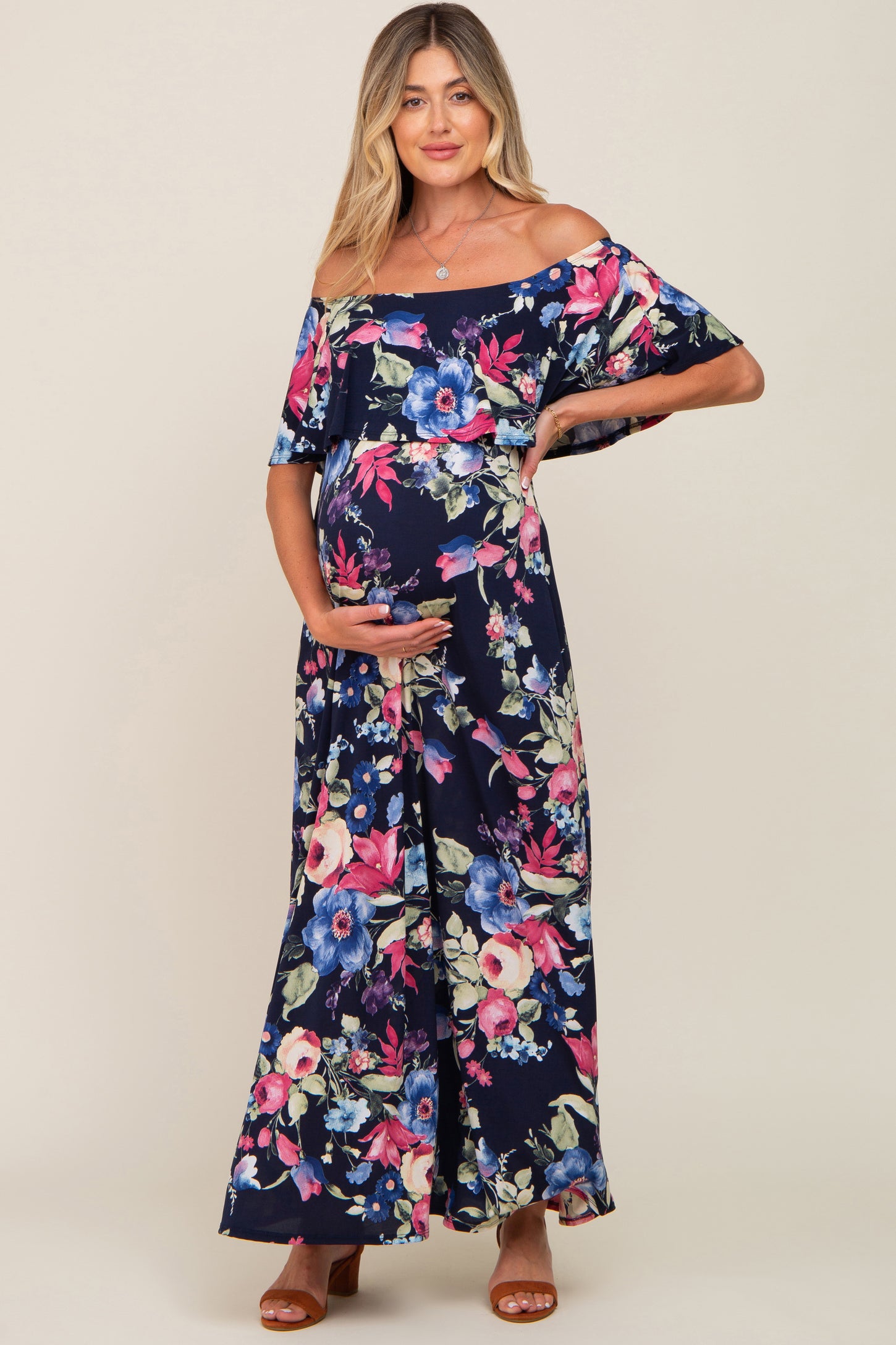 woman wearing a navy floral off-the-shoulder maternity maxi dress and holding her baby bump