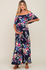 woman wearing a navy floral off-the-shoulder maternity maxi dress and holding her baby bump