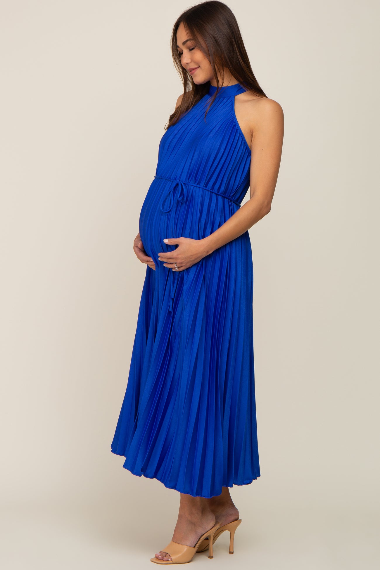 woman wearing a pleated royal blue maternity dress and holding her baby bump