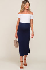 woman wearing a navy blue off-the-shoulder maternity dress with a white top and a side slit, holding a small handbag and showing her baby bump