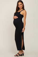 woman wearing a black ribbed maternity maxi dress with side slits, gently holding her baby bump