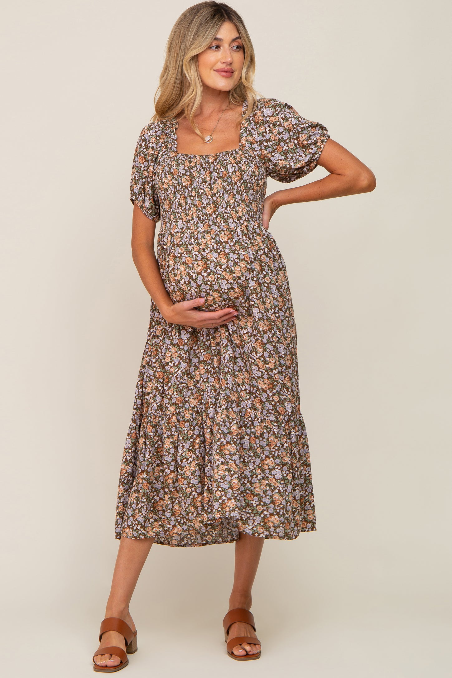 woman wearing a brown floral maternity dress with short puff sleeves and a square neckline, holding her baby bump