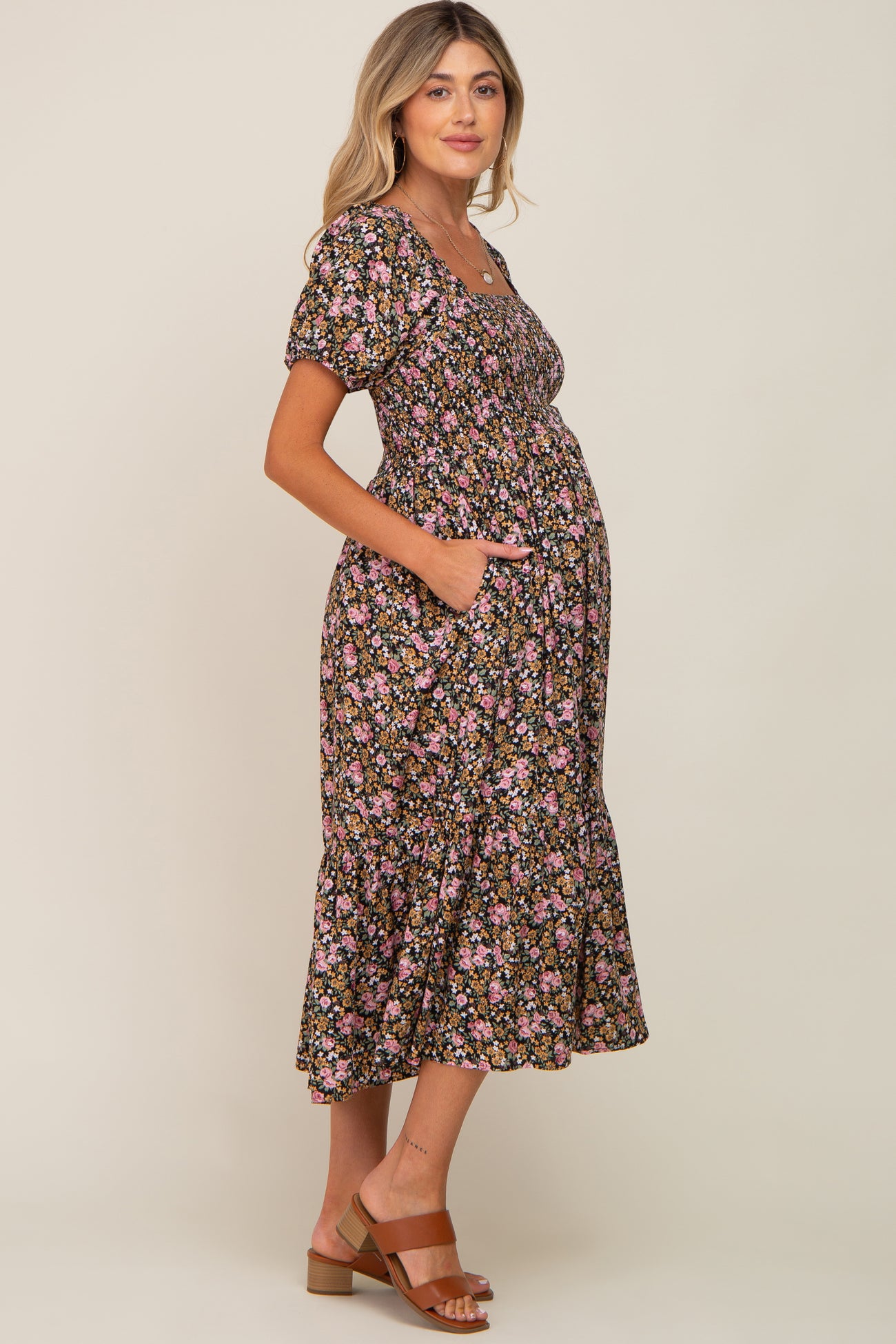 woman wearing a black floral maternity dress with puff sleeves and a tiered skirt, showing her baby bump and pockets