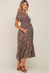 woman wearing a black floral maternity dress with puff sleeves and a tiered skirt, showing her baby bump and pockets