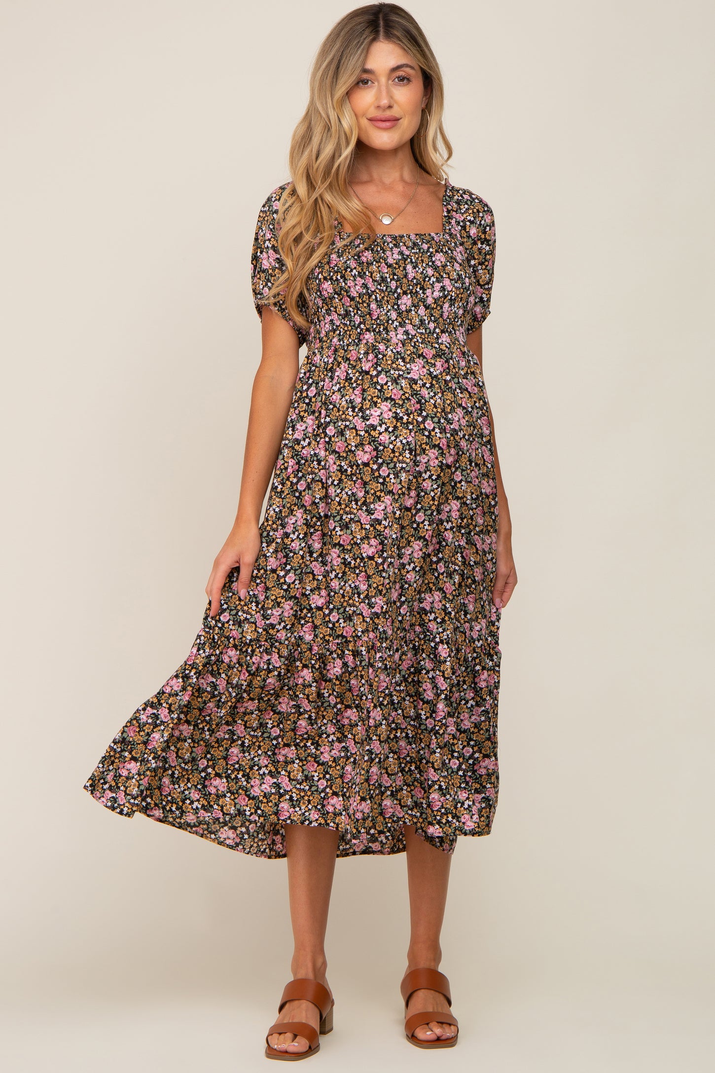 woman wearing a black floral maternity dress with short sleeves and a square neckline, highlighting her baby bump