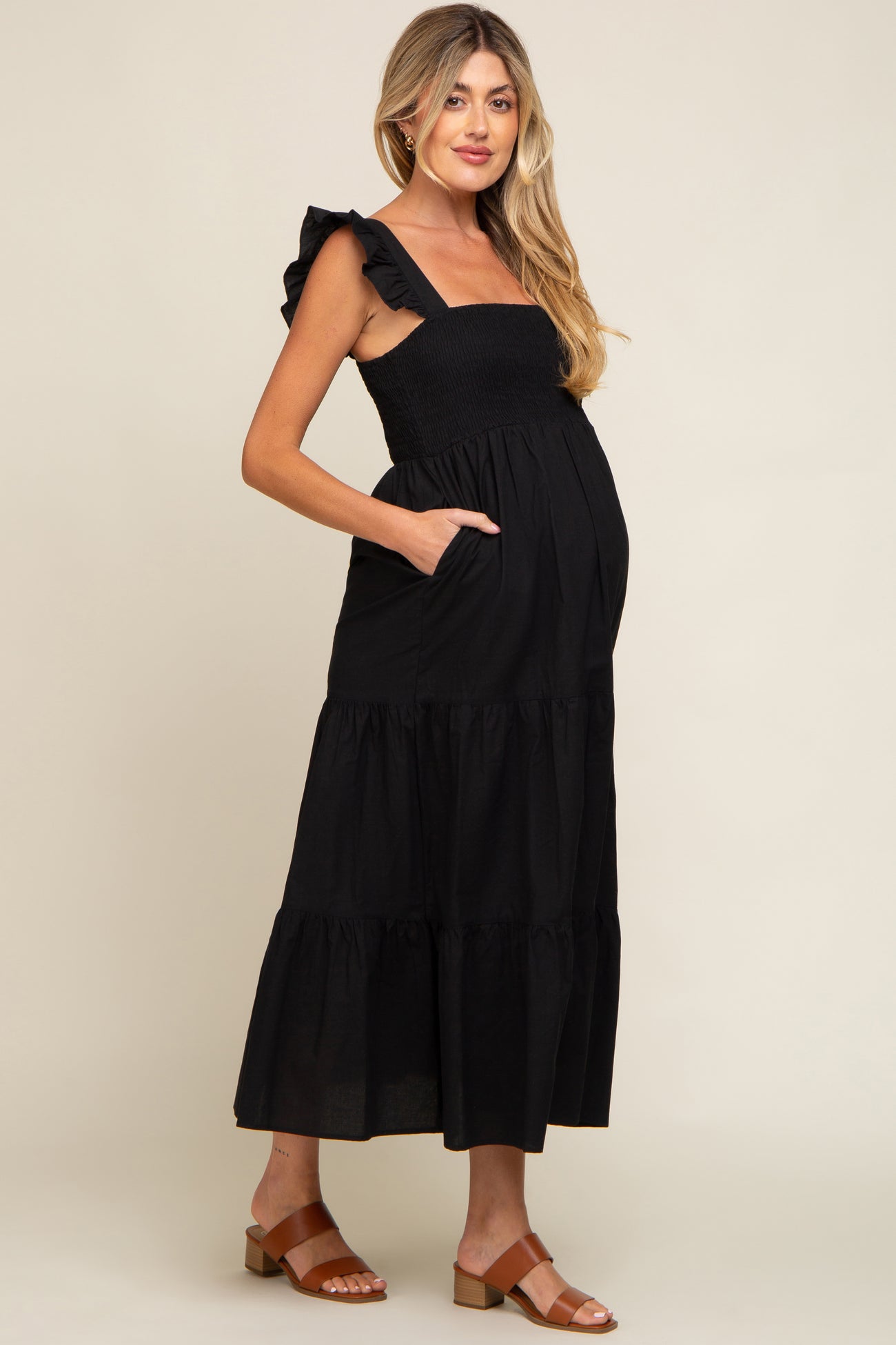 woman wearing a black maternity maxi dress with ruffle straps and pockets, showing her baby bump