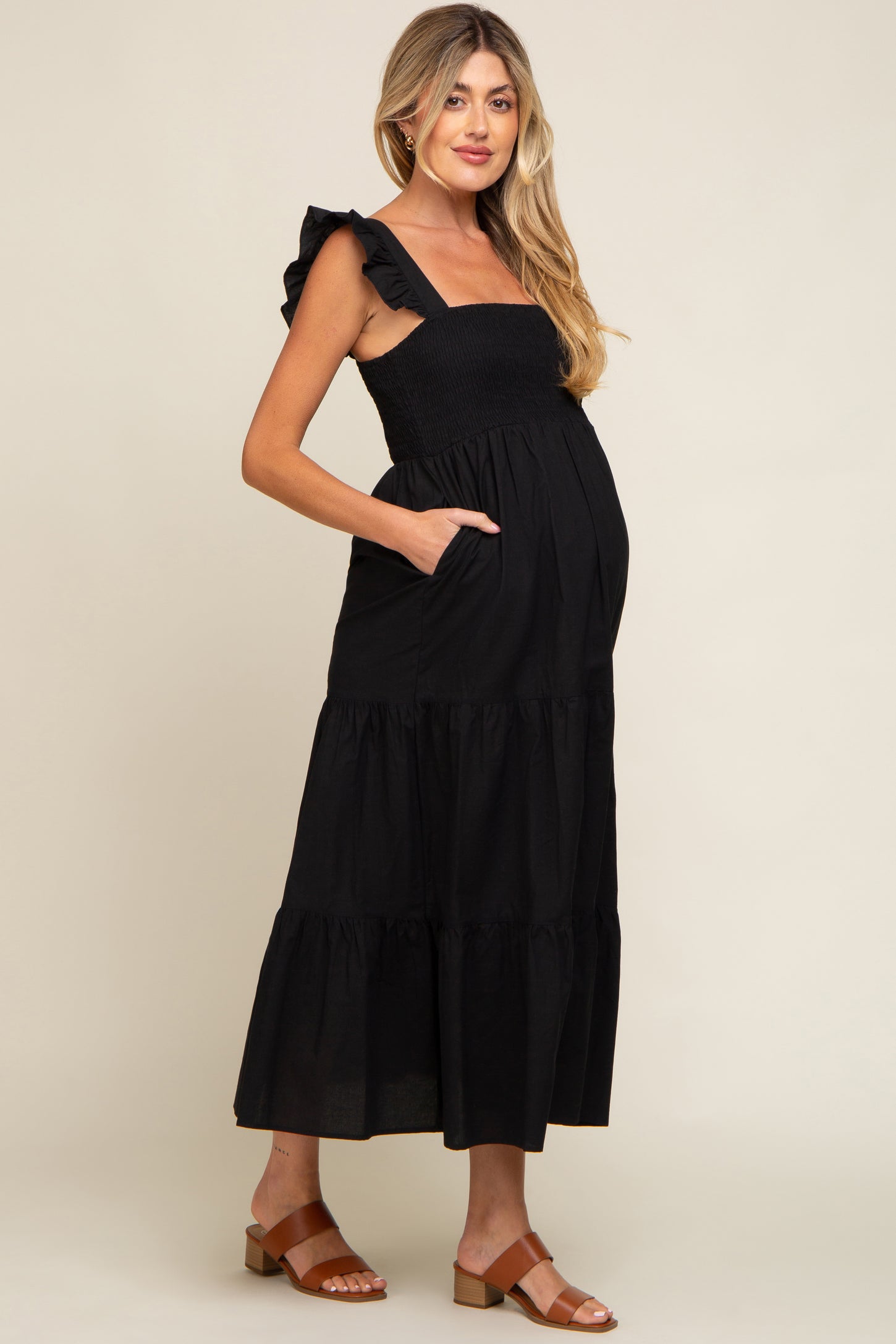 woman wearing a black maternity maxi dress with ruffle straps and pockets, showing her baby bump