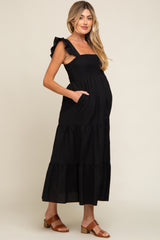 woman wearing a black maternity maxi dress with ruffle straps and pockets, showing her baby bump