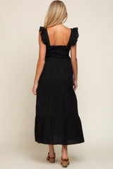 woman wearing a black maternity maxi dress with ruffled straps and a tiered skirt, showing her back
