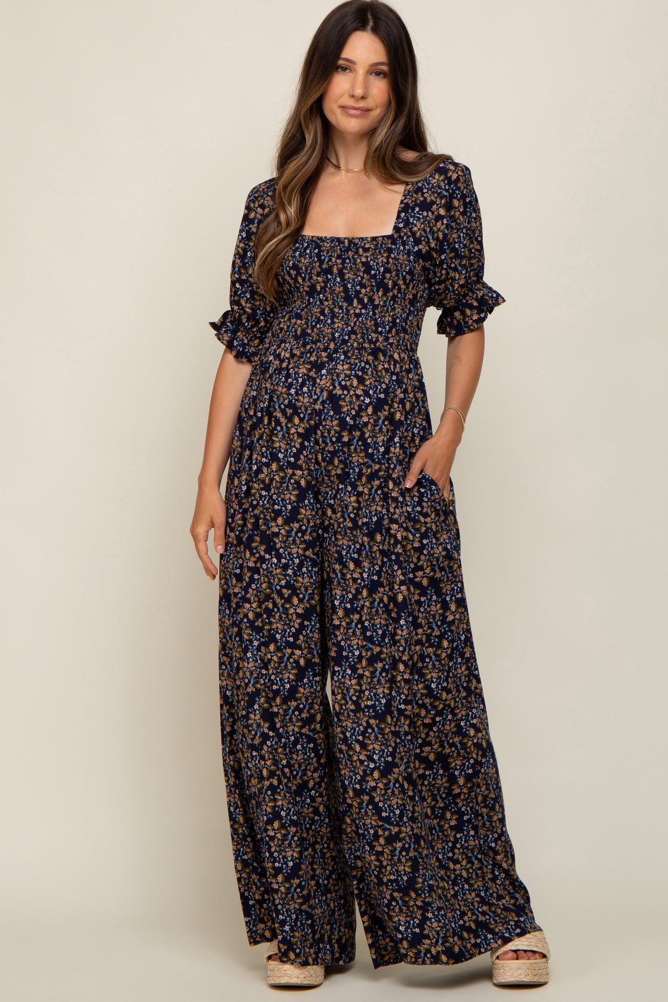 woman wearing a navy floral maternity jumpsuit with short puff sleeves and a square neckline, styled with platform sandals