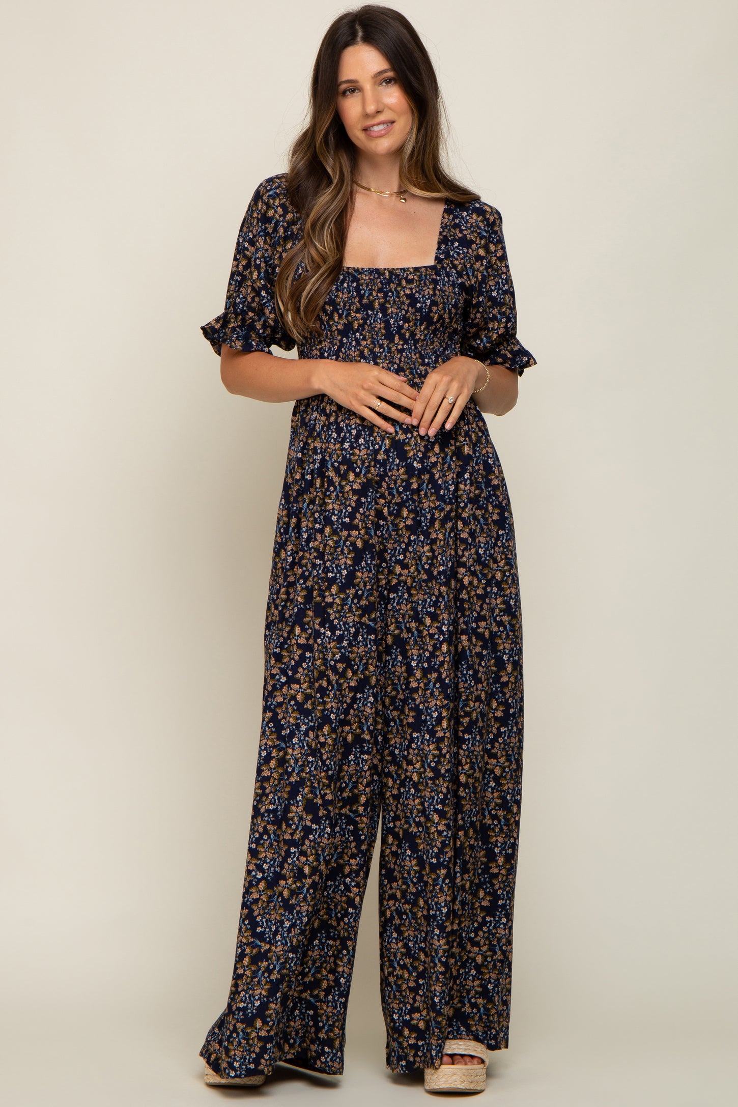 woman wearing a navy floral maternity jumpsuit with short sleeves and a square neckline, posing with a relaxed look