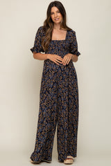 woman wearing a navy floral maternity jumpsuit with short sleeves and a square neckline, posing with a relaxed look