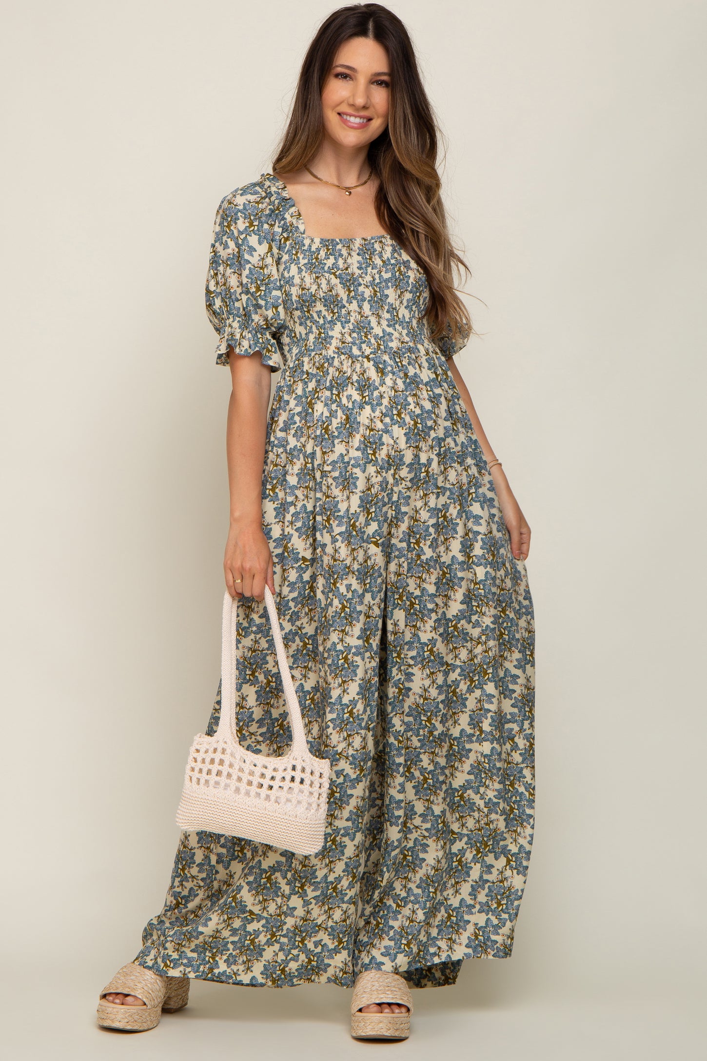 woman wearing a floral maternity maxi dress with puff sleeves and a square neckline, holding a white bag