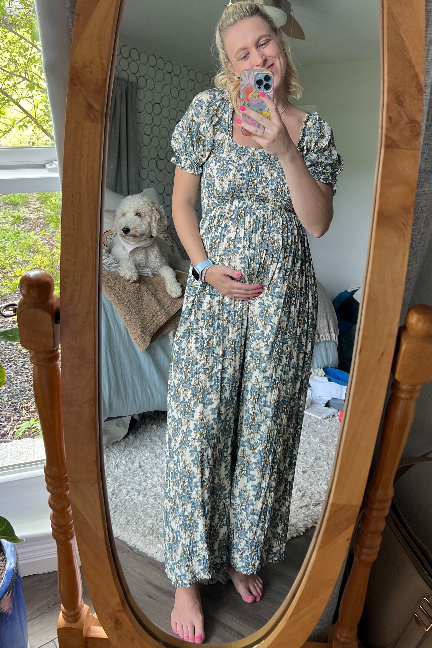 woman wearing a floral maternity maxi dress with puff sleeves and holding her baby bump in front of a mirror