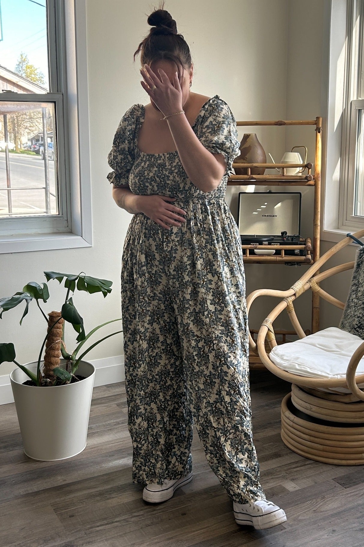 woman wearing a floral maternity jumpsuit and holding her baby bump while standing indoors