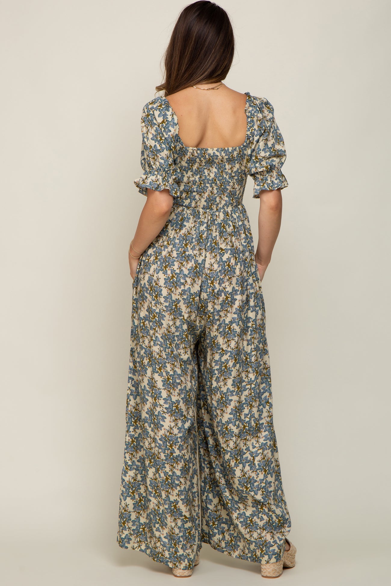 woman wearing a floral maternity jumpsuit with puffed sleeves and a loose fit, showcasing a pregnant belly from the back