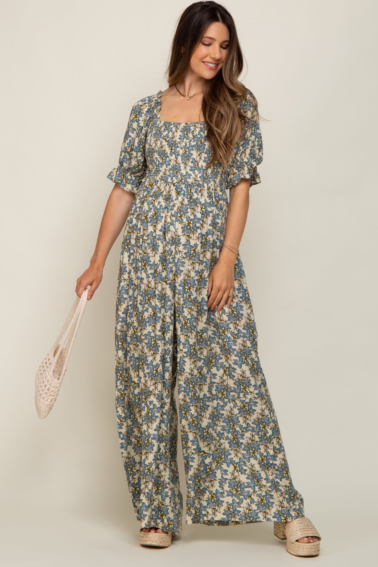 woman wearing a floral print maternity maxi dress with puff sleeves and a square neckline, holding a tote bag