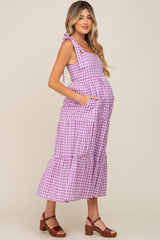 woman wearing a purple gingham maternity dress with tie straps and pockets, showing her baby bump
