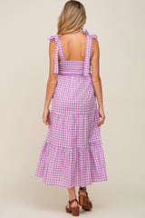 woman wearing a purple gingham maternity sundress with adjustable tie straps and a tiered skirt, showing her back