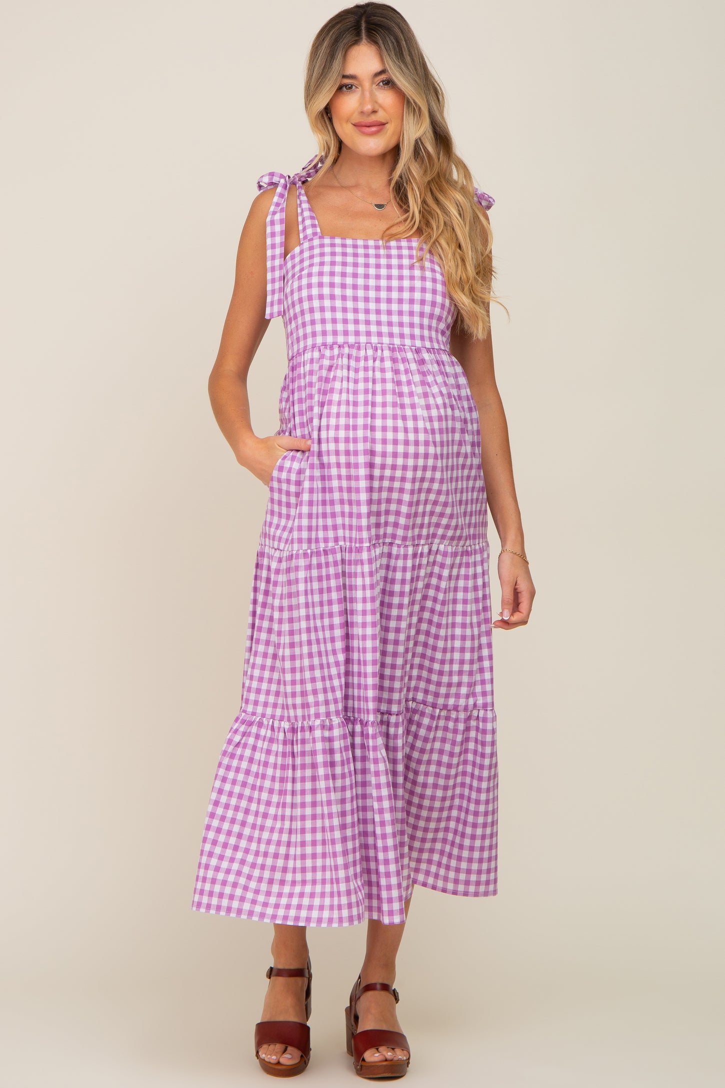 woman wearing a purple gingham maternity maxi dress with tie straps and pockets, showcasing her baby bump