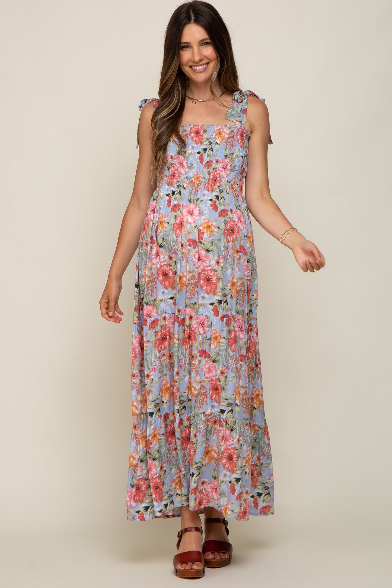 woman wearing a floral maternity maxi dress with tied shoulder straps and a flowing skirt, showing her baby bump