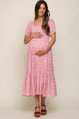 woman wearing a pink floral maternity dress with short sleeves and a tiered skirt, holding her baby bump