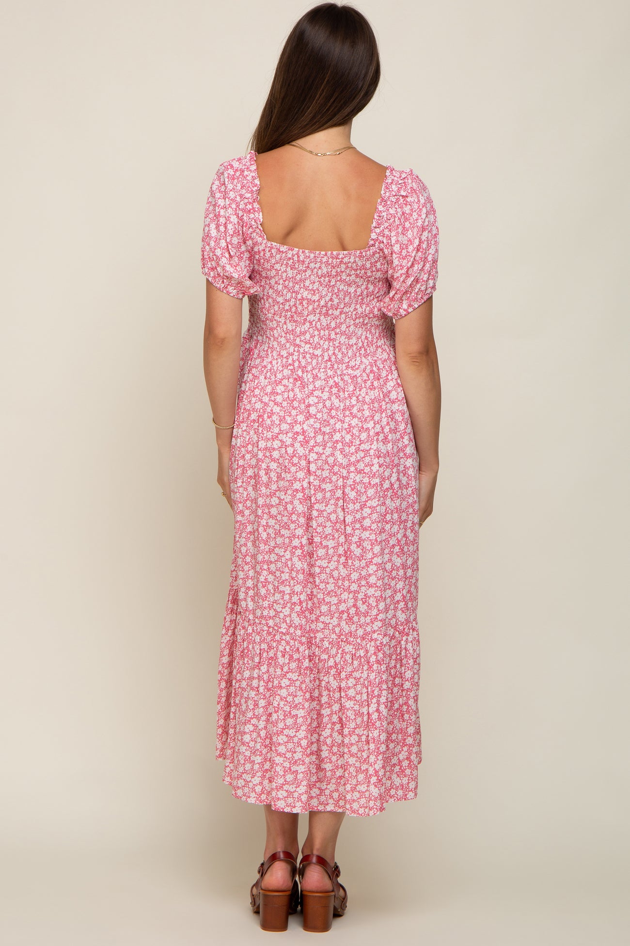 woman wearing a pink floral maternity maxi dress with puff sleeves and a tiered skirt, showing a baby bump