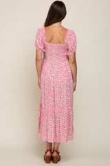woman wearing a pink floral maternity maxi dress with puff sleeves and a tiered skirt, showing a baby bump