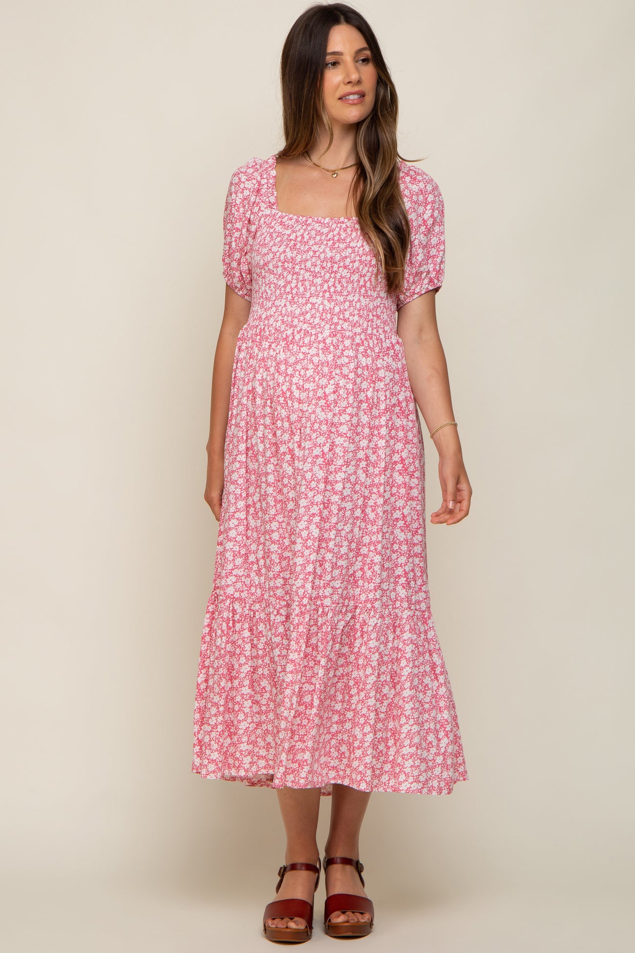 woman wearing a pink floral maternity dress with a square neckline and short puff sleeves, showing her baby bump