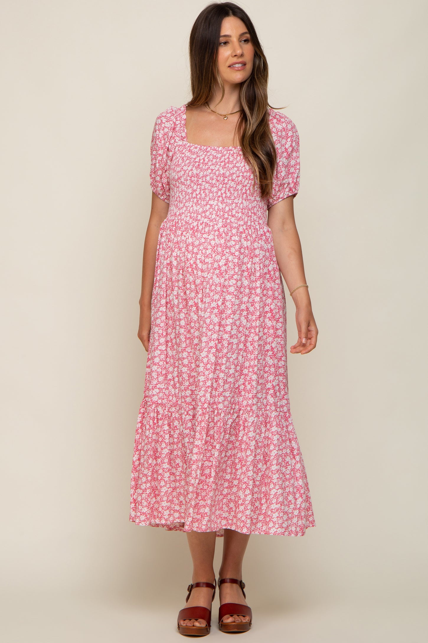 woman wearing a pink floral maternity dress with a square neckline and short puff sleeves, showing her baby bump