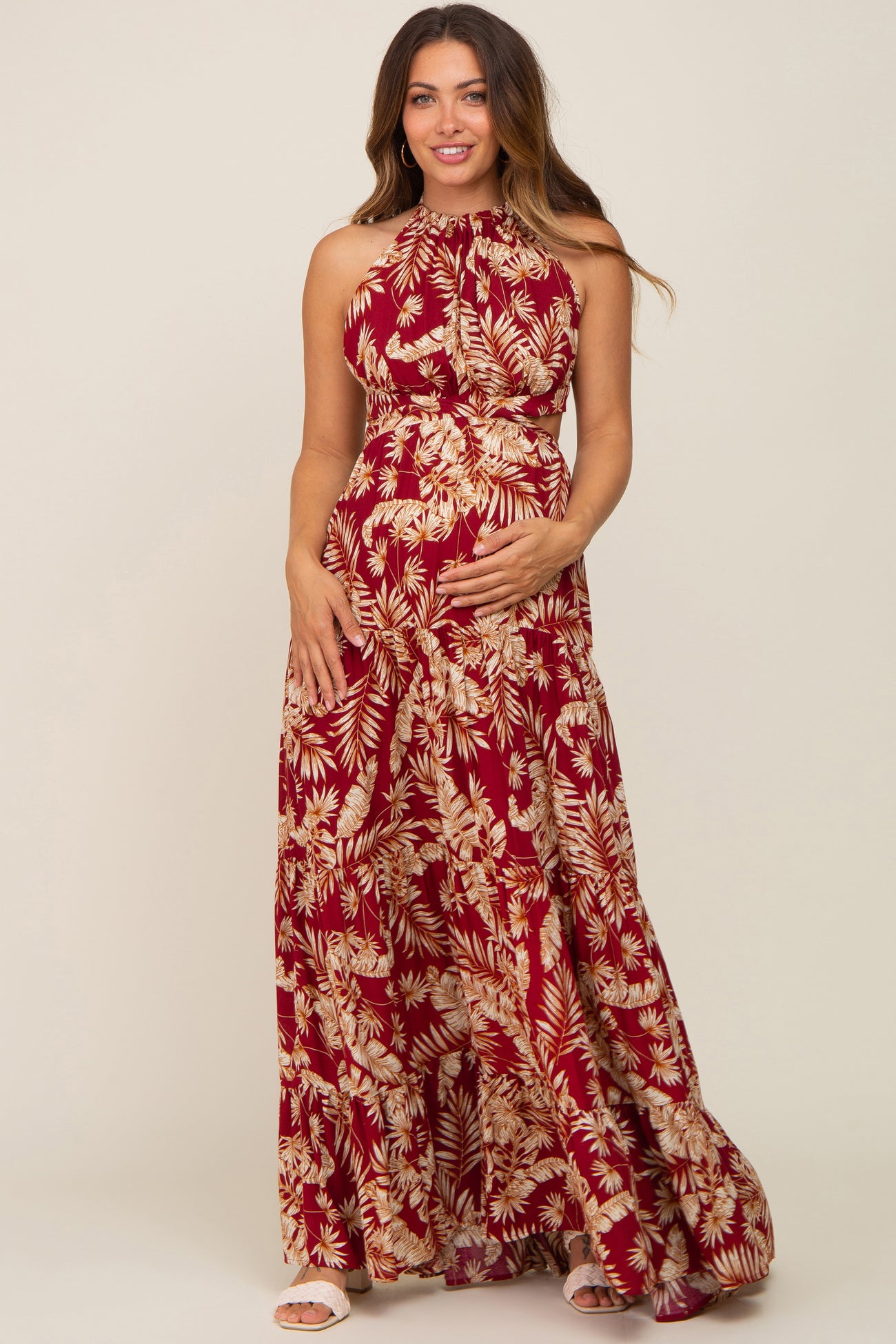 woman wearing a red floral halter neck maternity maxi dress and holding her baby bump