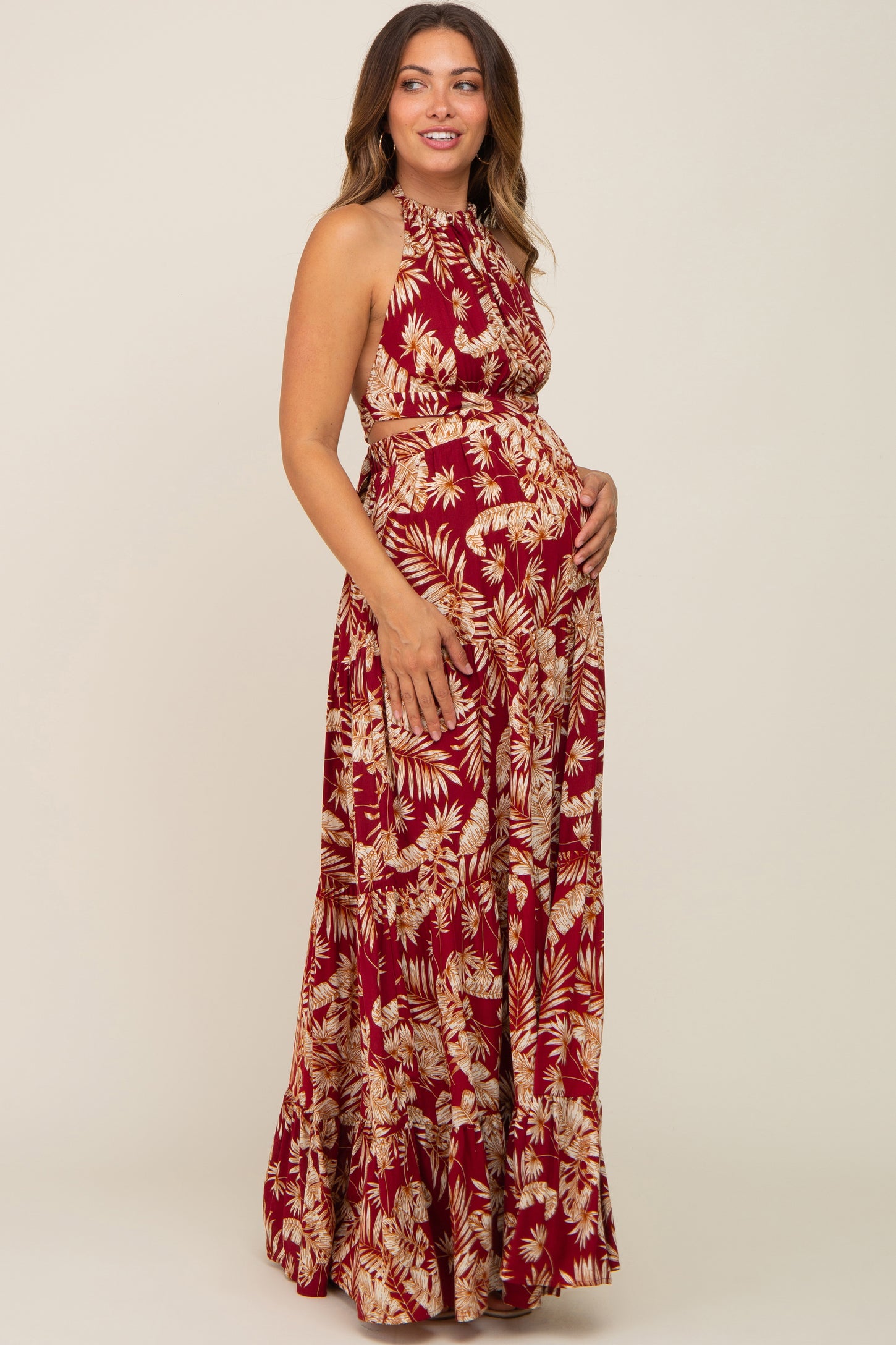 woman wearing a red and cream floral maternity maxi dress, showcasing her baby bump