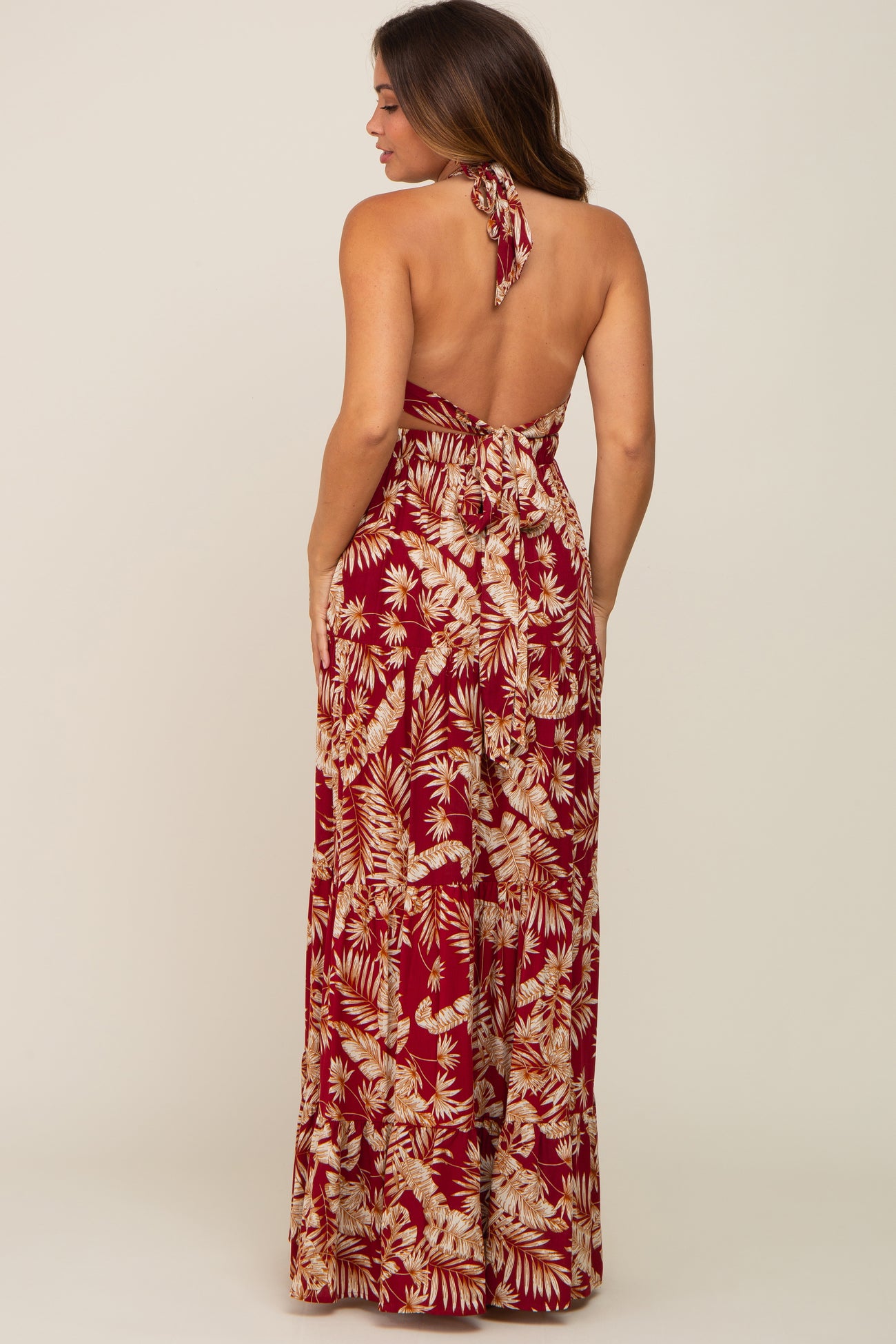 woman wearing a backless maternity maxi dress in burgundy with floral print and a halter tie detail