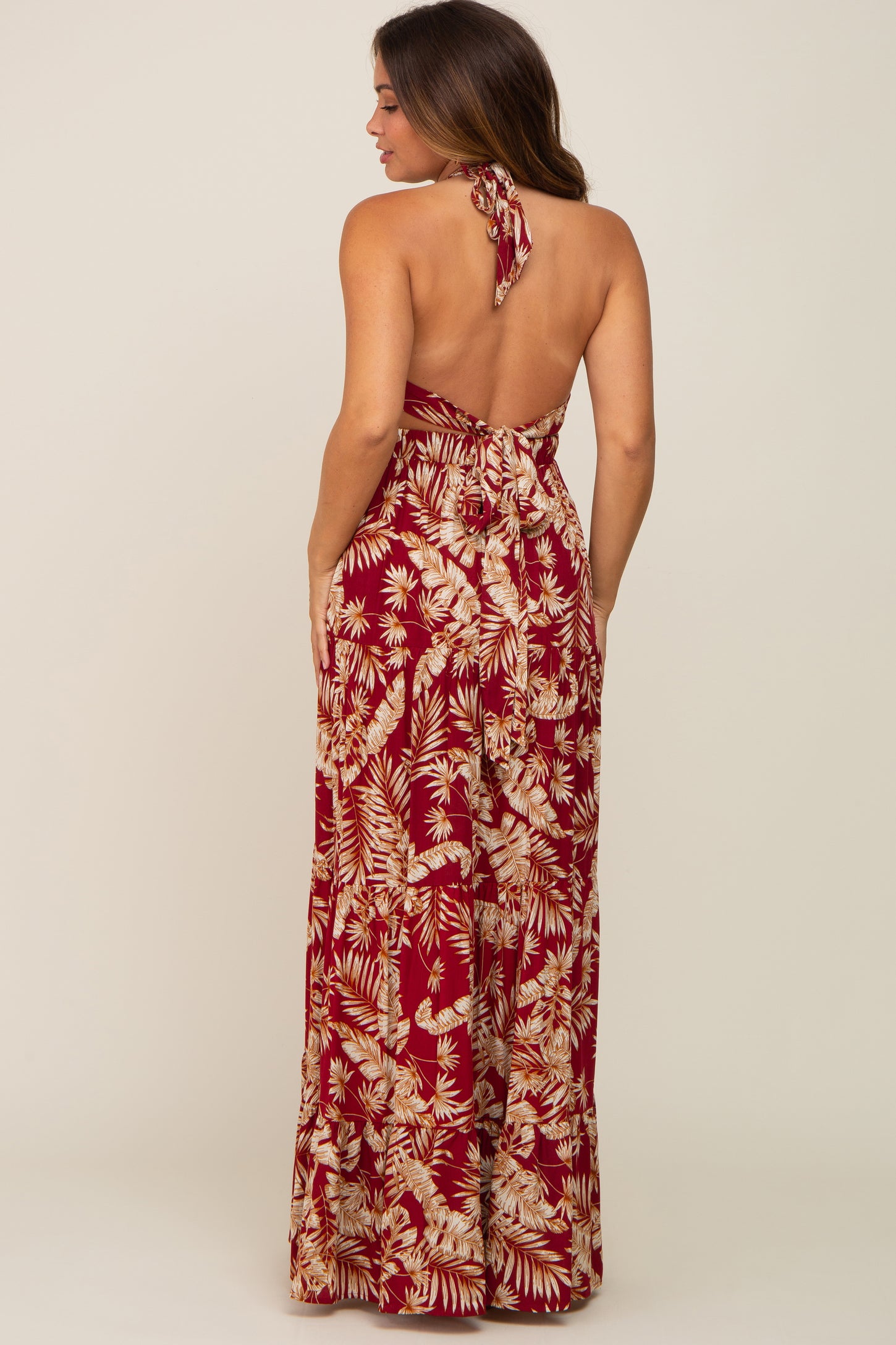 woman wearing a backless maternity maxi dress in burgundy with floral print and a halter tie detail