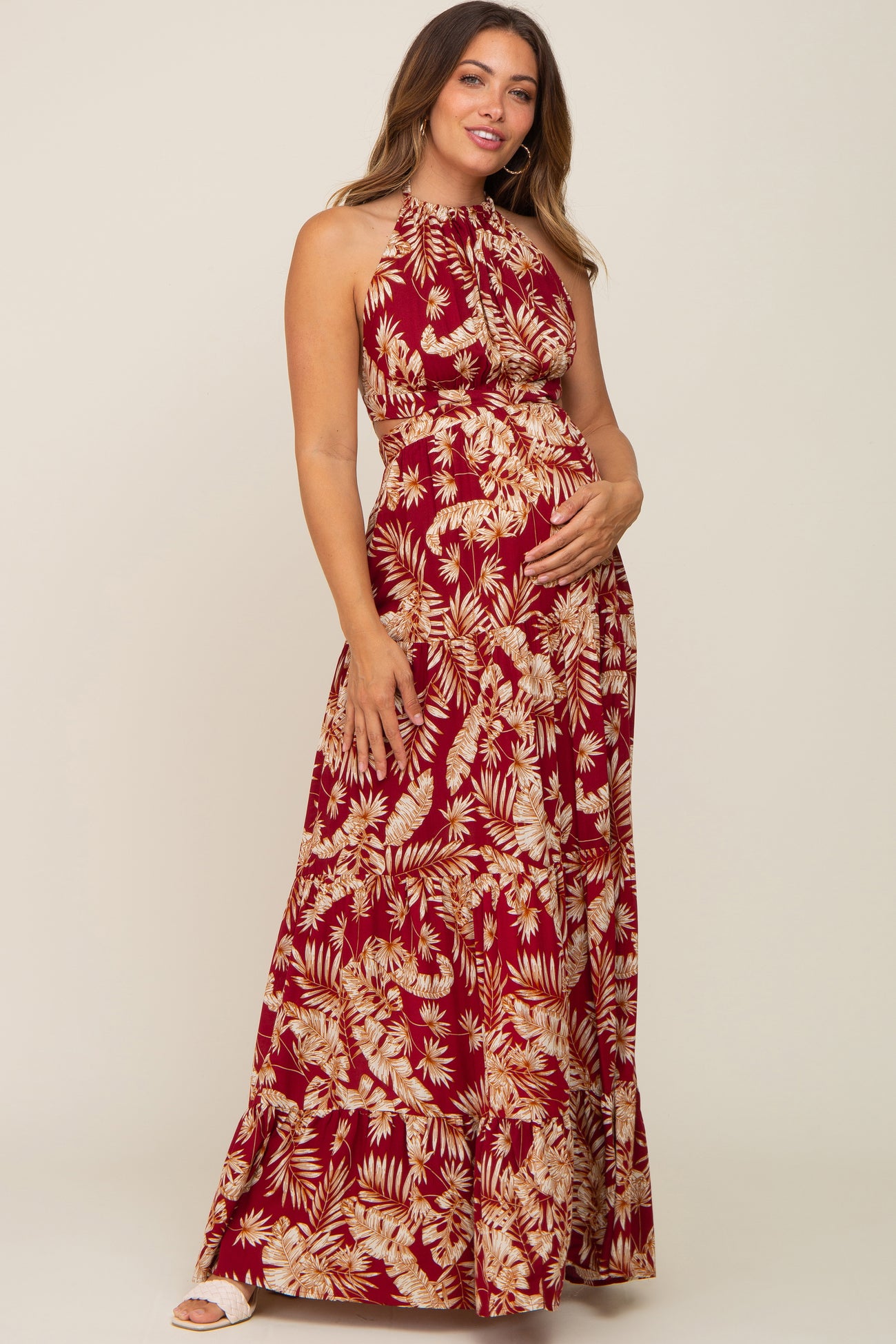 woman wearing a burgundy floral halter neck maternity maxi dress and cradling her baby bump
